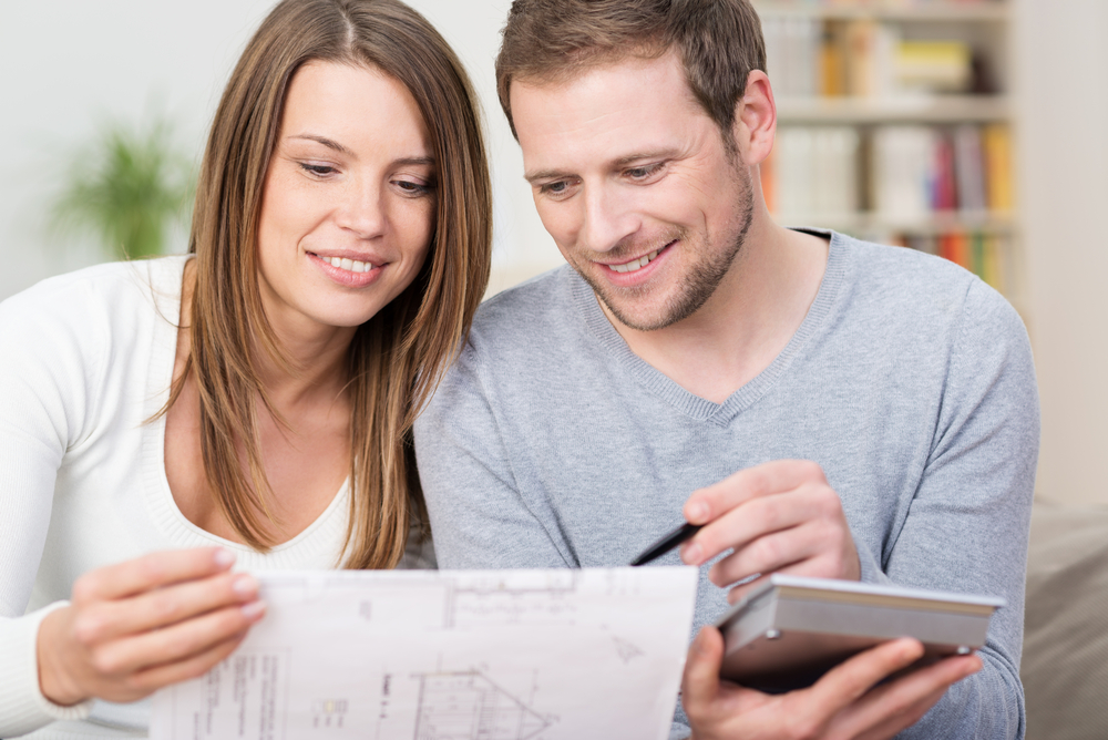 Young couple planning a new purchase sitting together pointing to a document held by the wife as the husband does the necessary calculations on a calculator